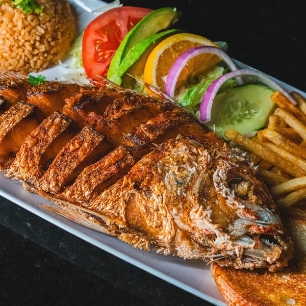 Crispy whole fried fish with rice, fries, and a fresh salad with avocado and orange slices.