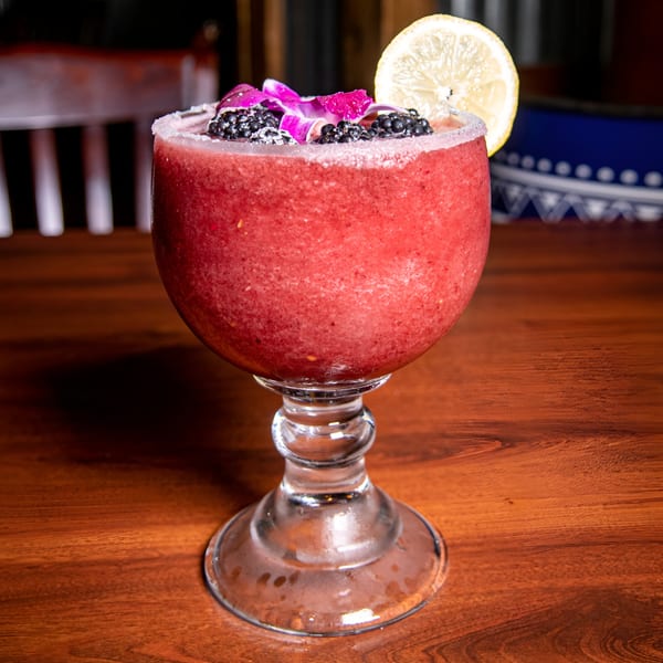 A vibrant red frozen drink, garnished with blackberries, a purple orchid, and a lemon slice.