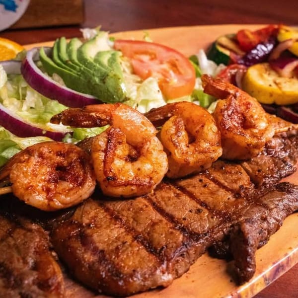 Grilled shrimp and steak with a side salad of avocado, lettuce, tomato, and red onion.