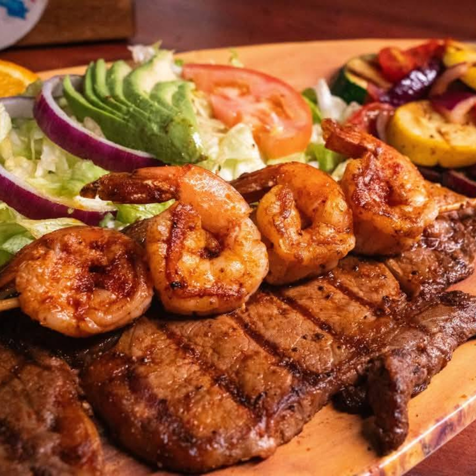 Grilled shrimp and steak with a side salad of avocado, lettuce, tomato, and red onion.