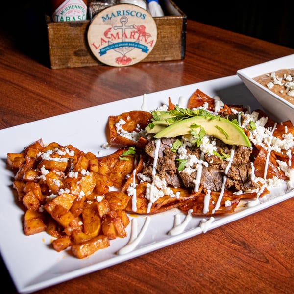 Chilaquiles with steak, avocado, and cheese, served with a side of refried beans.
