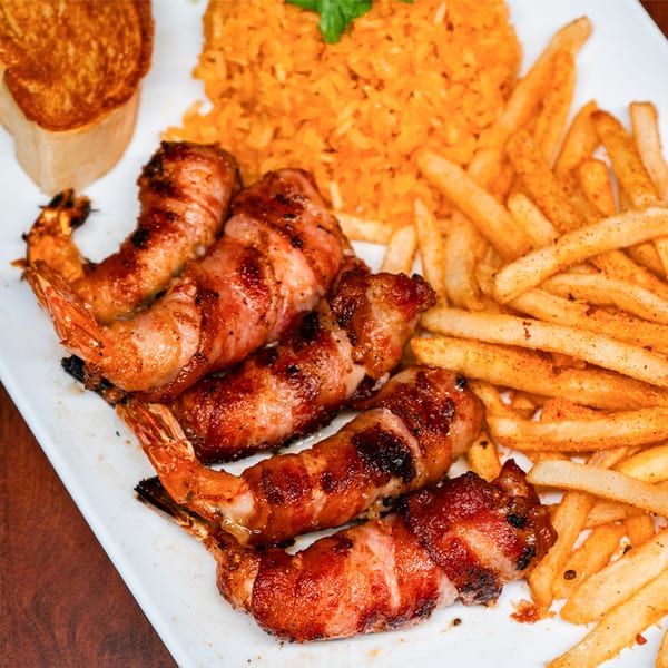Bacon-wrapped shrimp, seasoned fries, and orange rice with a piece of toast on a white plate.