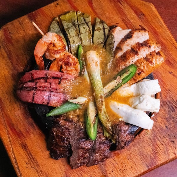 Grilled shrimp, chicken, steak, sausage, cheese, and vegetables with sauce on a wooden board.