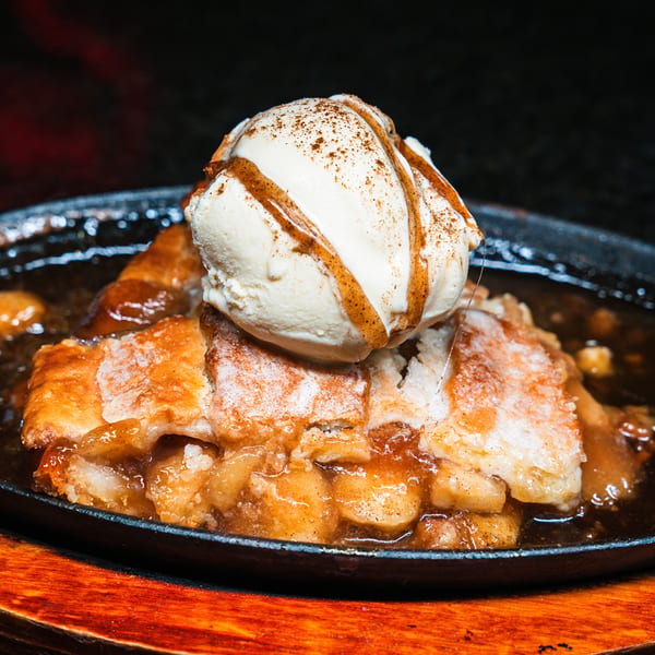 Warm apple pie with a scoop of vanilla ice cream drizzled with caramel and cinnamon.