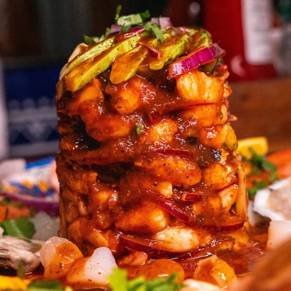 A tall seafood tower of shrimp, red onion, and avocado, drenched in a rich red sauce.