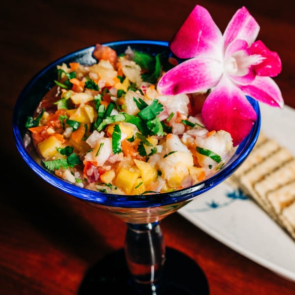 Mariscos La Marina's vibrant seafood ceviche in a blue glass, garnished with a pink orchid.