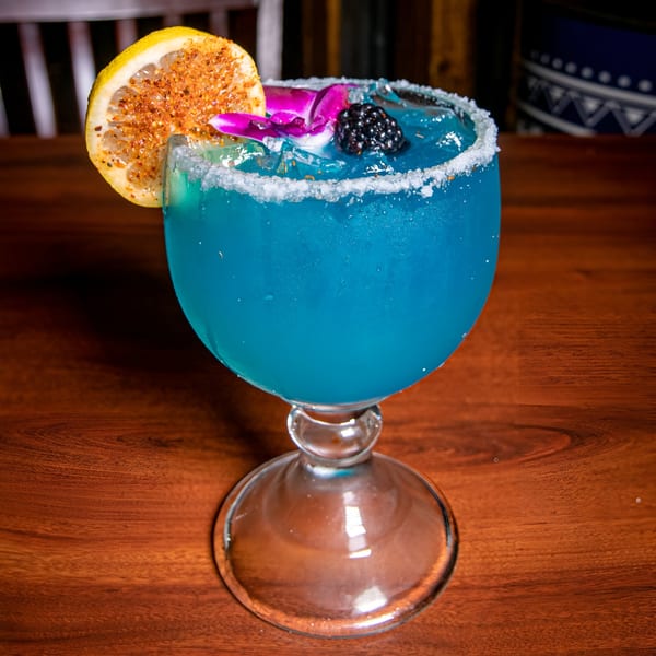 Blue margarita with a salted rim, garnished with a lime slice, blackberry, and purple orchid.